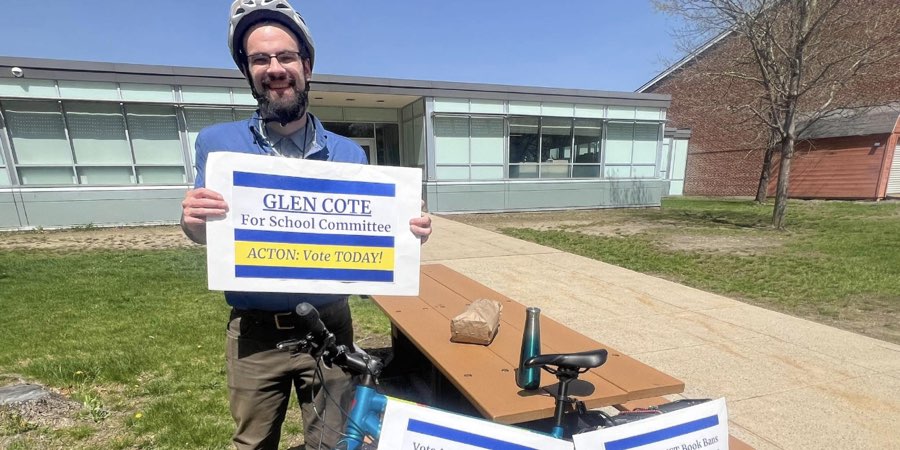 Glen Cote wearing a helmet holding a sign for his successful campaign for school committee member with his bike