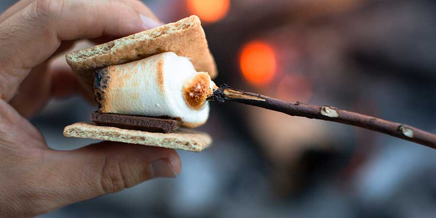 Hand holding a Smore, graham cracker with chocoloate and roasted marshmallow